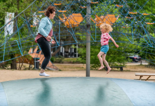 Volwassene en kind springen samen op een luchtkussen bij een vakantiepark met glamping accommodatie.