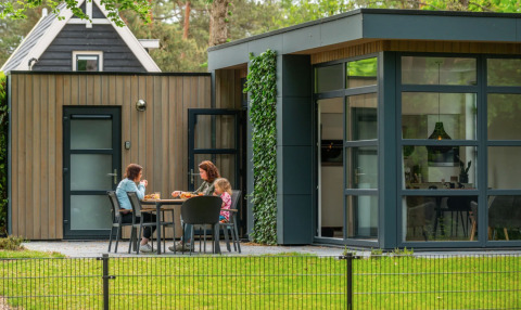 Moderne glamping accommodatie bij een vakantiepark met drie mensen die buiten ontspannen en eten.
