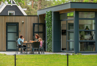 Moderne glamping accommodatie bij een vakantiepark met drie mensen die buiten ontspannen en eten.