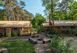 Glamping accommodatie in een vakantiepark met luxe tenten, houten terrassen en zitplaatsen buiten in het bos.