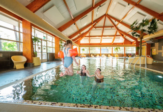 Kind met zwembandjes springt in een binnenzwembad bij een vakantiepark met glamping accommodaties.