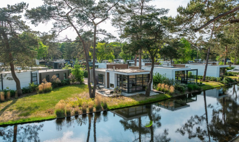 Luxe glamping accommodaties in een vakantiedomein met moderne huisjes aan het water en veel groen.