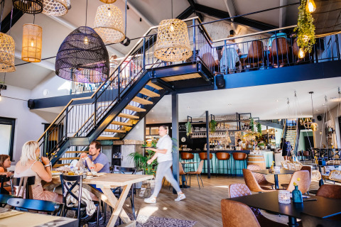 Modern restaurantinterieur met houten meubels, sfeerverlichting en gasten in Papillon Country Resort.