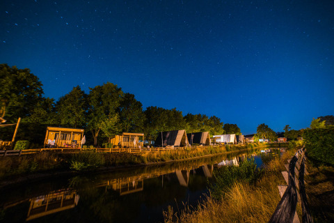 Verlichte houten huisjes bij nacht aan een waterkant in Papillon Country Resort, Overijssel, Nederland.