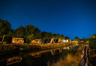 Verlichte houten huisjes bij nacht aan een waterkant in Papillon Country Resort, Overijssel, Nederland.
