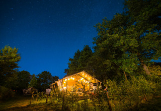 Verlichte tent onder een heldere sterrenhemel bij Papillon Country Resort, omringd door bomen in Overijssel.