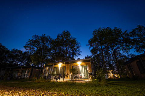 Verlichte houten huisjes bij nacht in Papillon Country Resort, vakantiepark omringd door bomen in Overijssel.