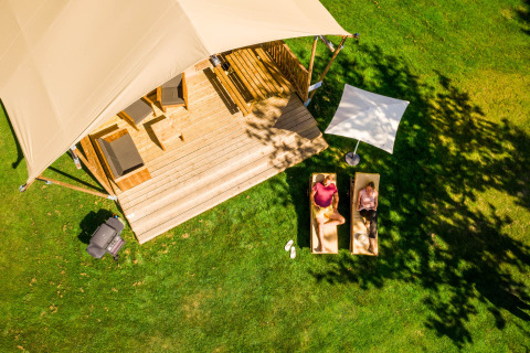 Luchtfoto van een glampingtent bij Papillon Country Resort met twee mensen ontspannen op ligstoelen in het gras.