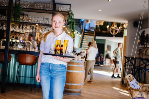 Jonge serveerster met dienblad vol drankjes in het gezellige restaurant van Papillon Country Resort.