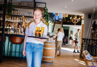 Jonge serveerster met dienblad vol drankjes in het gezellige restaurant van Papillon Country Resort.