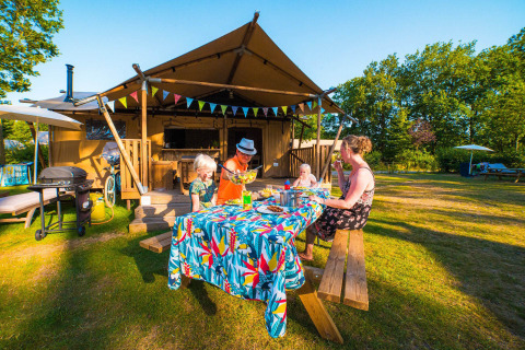 Gezin geniet van een zomerse maaltijd buiten bij een glampingtent op Papillon Country Resort, Overijssel.