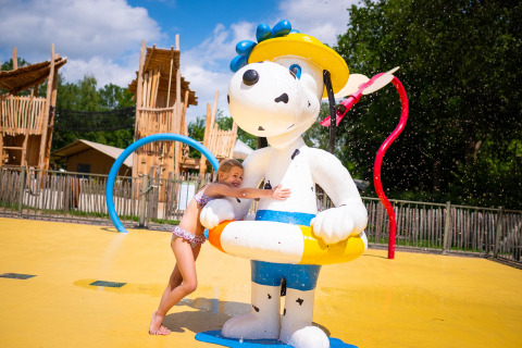 Een meisje knuffelt een groot hondenbeeld met gele zwemband bij het waterspeelpark in Papillon Country Resort.