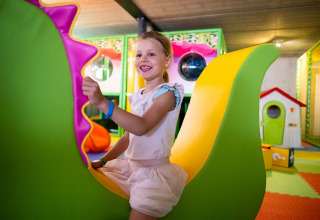 Kind speelt vrolijk op kleurrijk speeltoestel in binnenspeeltuin van Papillon Country Resort, Overijssel.