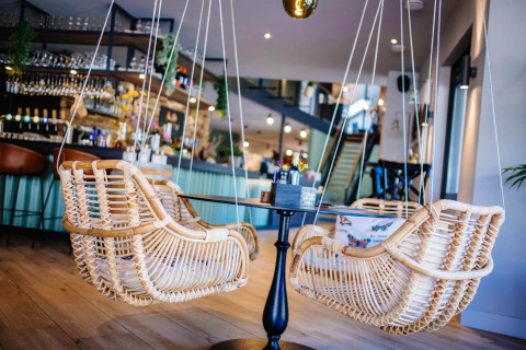 Hippe houten schommelstoelen aan een ronde tafel in een modern café bij Papillon Country Resort.