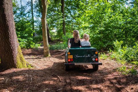 Twee kinderen rijden in een kleine jeep door een bosrijk pad bij Papillon Country Resort in Overijssel.