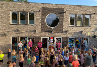 Kinderen en gezinnen verzamelen zich buiten voor een optreden met een mascotte bij Papillon Country Resort.