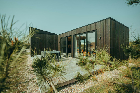Lodge moderno de madera negra con terraza en Holiday park De Klepperstee, Países Bajos, rodeado de naturaleza.