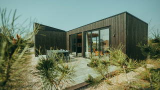 Lodge moderno de madera negra con terraza en Holiday park De Klepperstee, Países Bajos, rodeado de naturaleza.