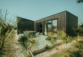 Moderne zwarte lodge met terras op vakantiepark De Klepperstee in Nederland, omgeven door natuur.