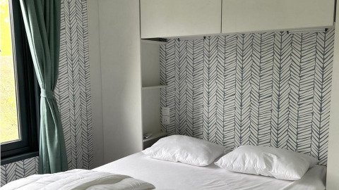 Dormitorio en Bungalow Cottage Prestige en Papillon Country Resort con papel tapiz moderno y cortina verde.