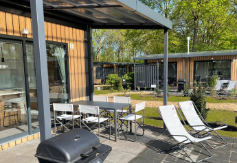 Terraza exterior con mesa, sillas, tumbonas y barbacoa en Bungalow Cottage Prestige del Papillon Country Resort.