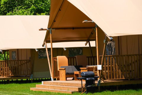 Tienda safari Comfort con porche de madera y tumbonas en Papillon Country Resort, Países Bajos, naturaleza.