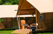 Tienda safari Comfort con porche de madera y tumbonas en Papillon Country Resort, Países Bajos, naturaleza.