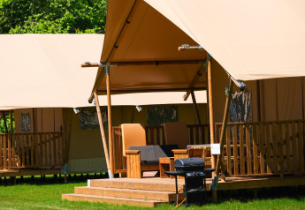 Safari-Zelt Comfort mit Holzveranda und Relaxsessel im Papillon Country Resort, Niederlande, Grünbereich.