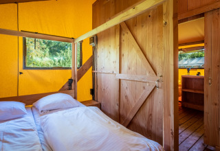 Dormitorio en Safari tent Comfort en Papillon Country Resort, Países Bajos, con paredes de madera y lona amarilla.
