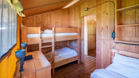 Habitación de madera en un lodge con litera, cama individual, muebles de madera y ventana soleada.