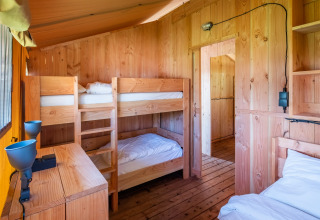 Habitación de madera en un lodge con litera, cama individual, muebles de madera y ventana soleada.
