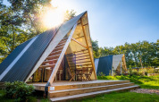 Moderne A-formet tiny house på Papillon Country Resort i Holland med træterrasse og morgensol.