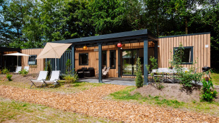 Cottage Next XXL Family Deluxe lodge op Papillon Country Resort, Nederland, met terras tussen het groen.