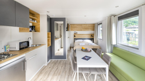 Interior de tiny house moderno y luminoso con cocina, mesa, cama y sofá verde en Papillon Country Resort, Países Bajos.