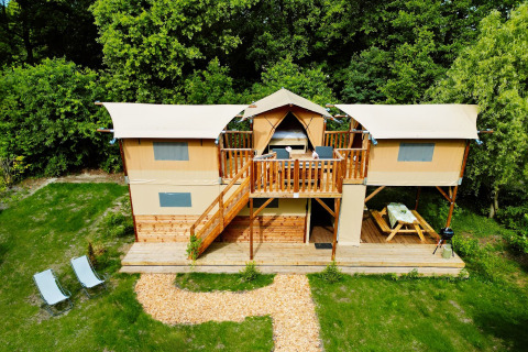 Twee verdiepingen tellende Air Dreamer 3 Deluxe lodge met terras en picknickbank, omgeven door bomen.