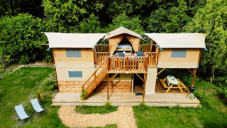 Twee verdiepingen tellende Air Dreamer 3 Deluxe lodge met terras en picknickbank, omgeven door bomen.