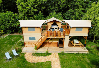 Air Dreamer 3 Deluxe lodge met twee verdiepingen, terrasstoelen, picknicktafel en omringd door bomen.