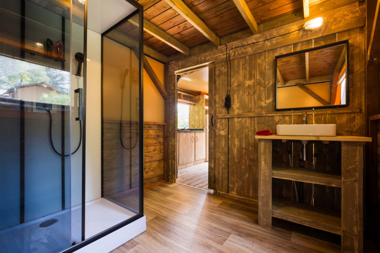 Baño rústico con ducha de cristal y detalles de madera en Air Dreamer 3 Deluxe, Papillon Country Resort.