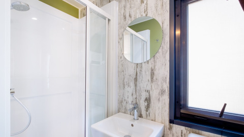 Moderne badkamer met douche, ronde spiegel en lavabo in Fish Cabin Deluxe, Papillon Country Resort, Nederland.
