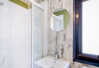 Moderne badkamer met douche, ronde spiegel en lavabo in Fish Cabin Deluxe, Papillon Country Resort, Nederland.