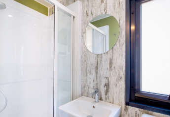 Baño moderno con ducha, espejo redondo y lavabo en Fish Cabin Deluxe, Papillon Country Resort, Países Bajos.
