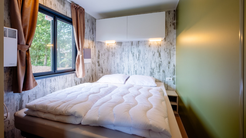 Modern bedroom in Fish Cabin Deluxe at Papillon Country Resort, Netherlands, with double bed and window.