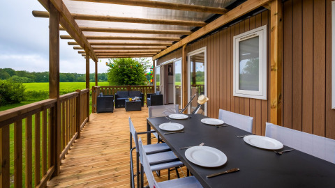 Terraza de madera con mesa de comedor y zona lounge en Cottage Next XL, Papillon Country Resort, Países Bajos.