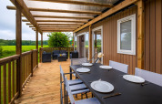 Terraza de madera con mesa de comedor y zona lounge en Cottage Next XL, Papillon Country Resort, Países Bajos.
