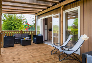 Terraza de madera en Cottage Next XL en Papillon Country Resort, Países Bajos, con muebles de salón y sillas.