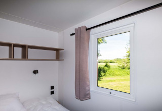 Dormitorio moderno en Fish Cabin en Papillon Country Resort con ventana y vista a la naturaleza verde.