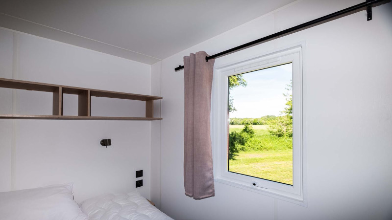 Dormitorio moderno en Fish Cabin en Papillon Country Resort con ventana y vista a la naturaleza verde.
