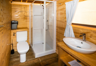 Badeværelse med træpaneler, bruser, toilet og vask på Air Lodge 2.0 i Papillon Country Resort, Holland.