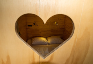 Uitzicht op een knus bed via een hartvormig raam bij Air Lodge 2.0, Papillon Country Resort, Nederland.