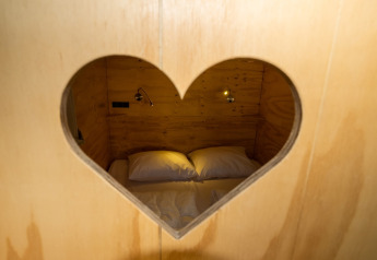 Gezicht op een knus bed door een hartvormig raam in Air Lodge 2.0, Papillon Country Resort, Nederland.